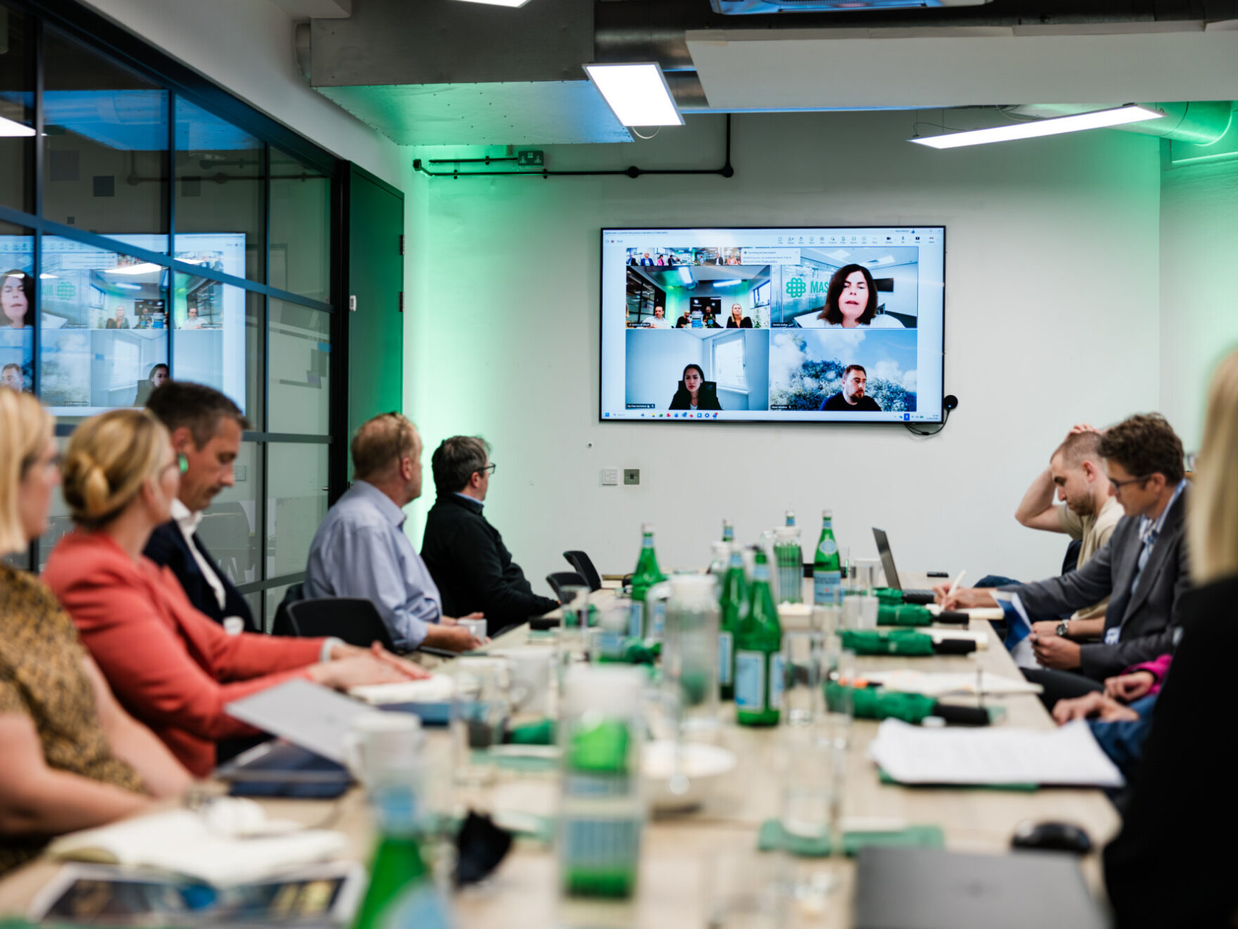Group working around a large meeting table with people also joining remotely on screen