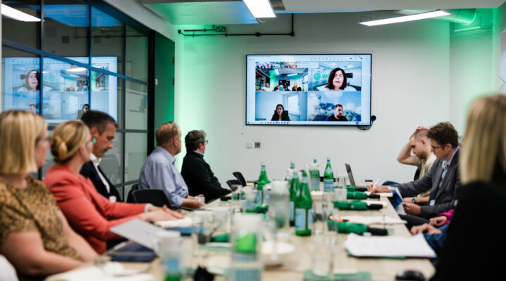 Group working around a large meeting table with people also joining remotely on screen
